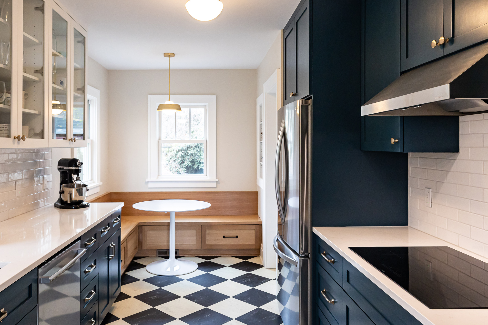 Galley kitchen with navy shaker cabinets, black and white checkerboard linoleum floor, white oak breakfast nook, and brass pendant, Stanton Street Kitchen remodel by Tweto Architecture