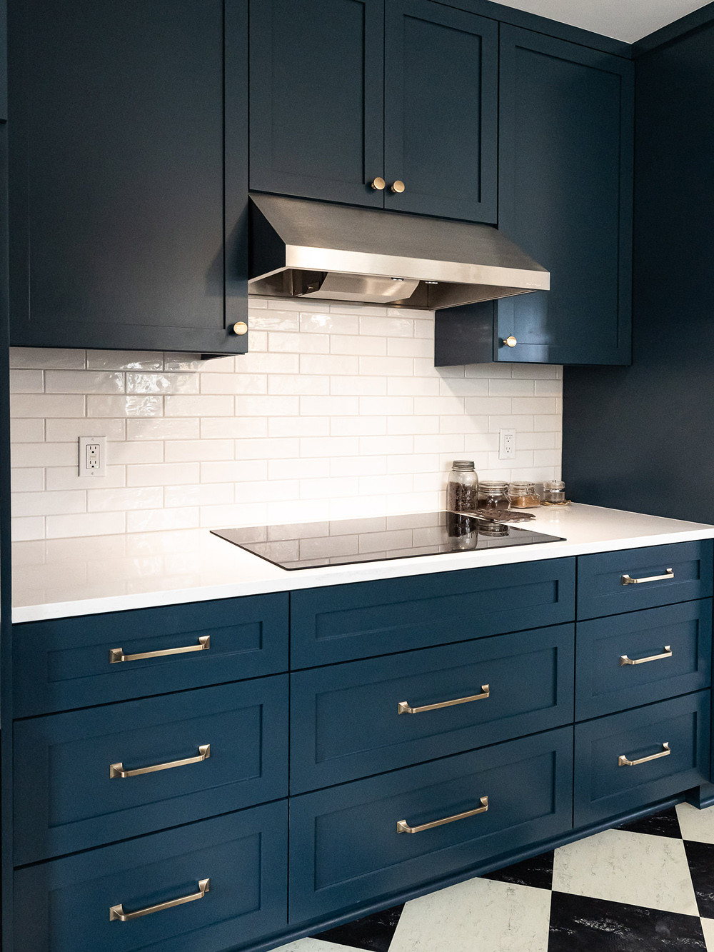 Range with induction cooktop, stainless range hood, navy shaker cabinetry with brass hardware, and white subway tile backsplash, Stanton Street Kitchen by Tweto Architecture