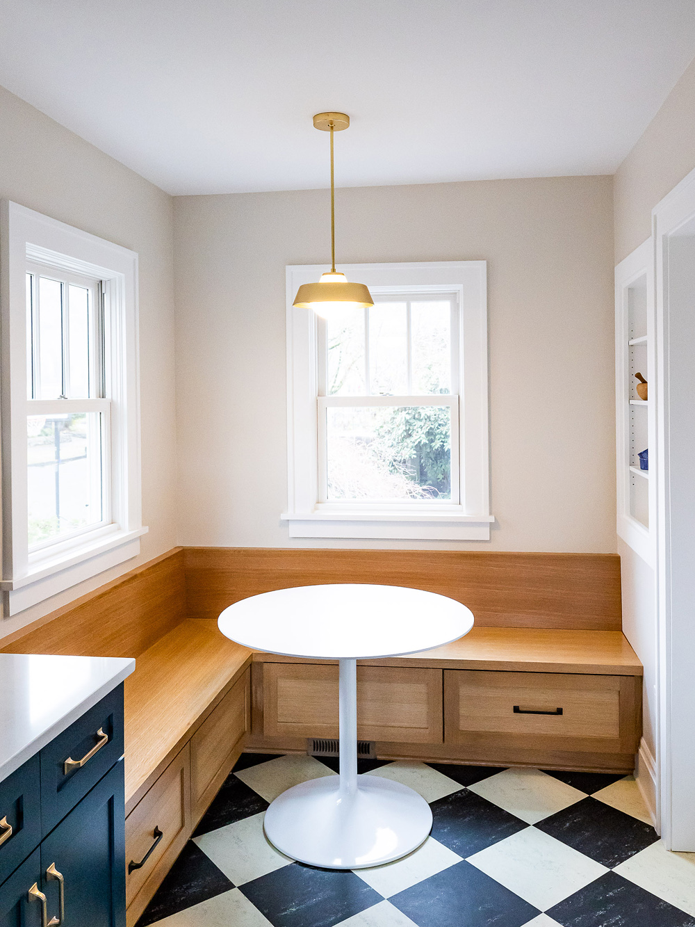White oak L-shaped built-in breakfast nook with storage drawers, round tulip table, and brass pendant above east-facing window, Stanton Street Kitchen by Tweto Architecture
