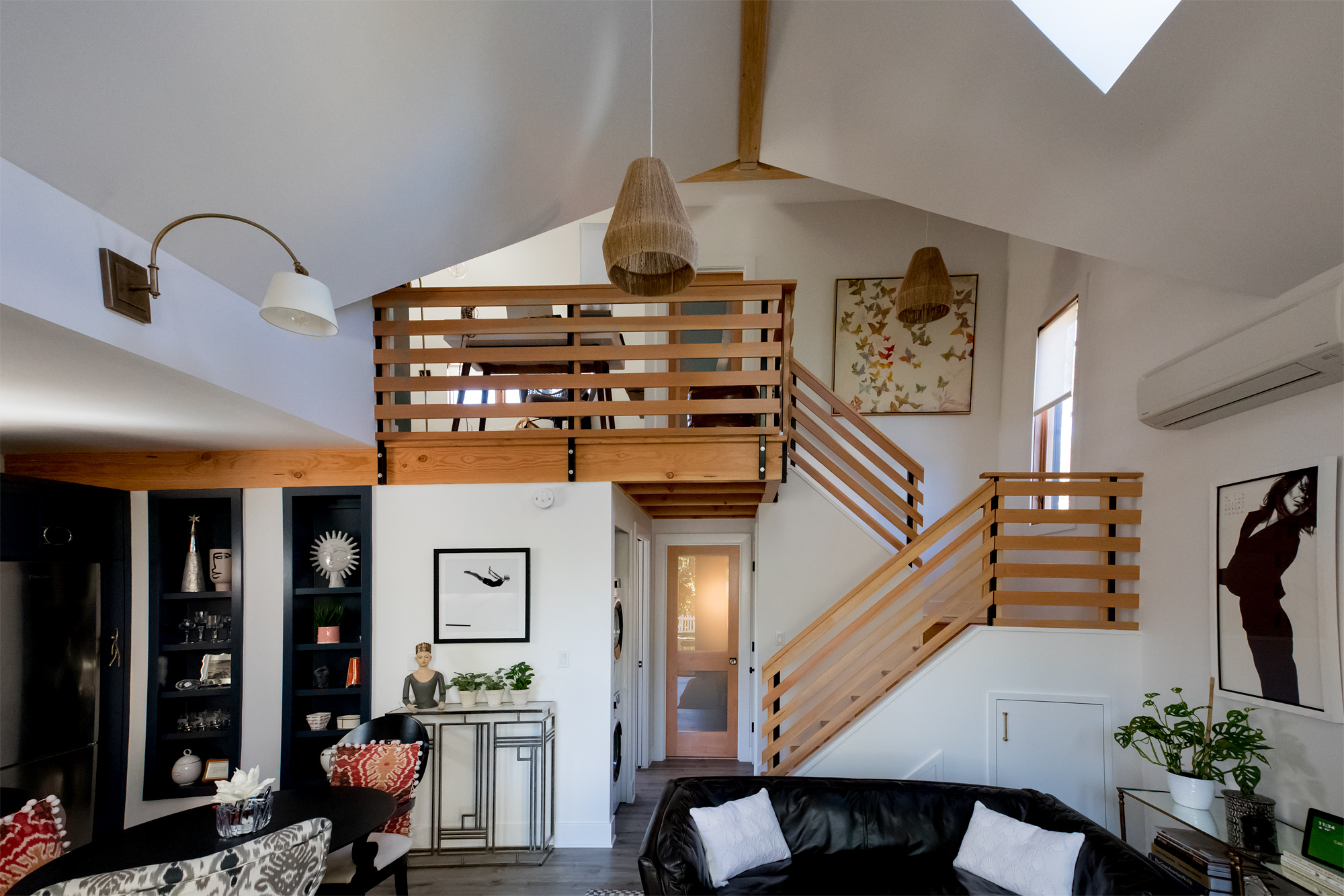 Wide interior view showing the full height of the great room, wood slatted loft railing, stair to the loft, vaulted ceiling with ridge beam, and built-in shelving, Vancouver Avenue ADU by Tweto Architecture