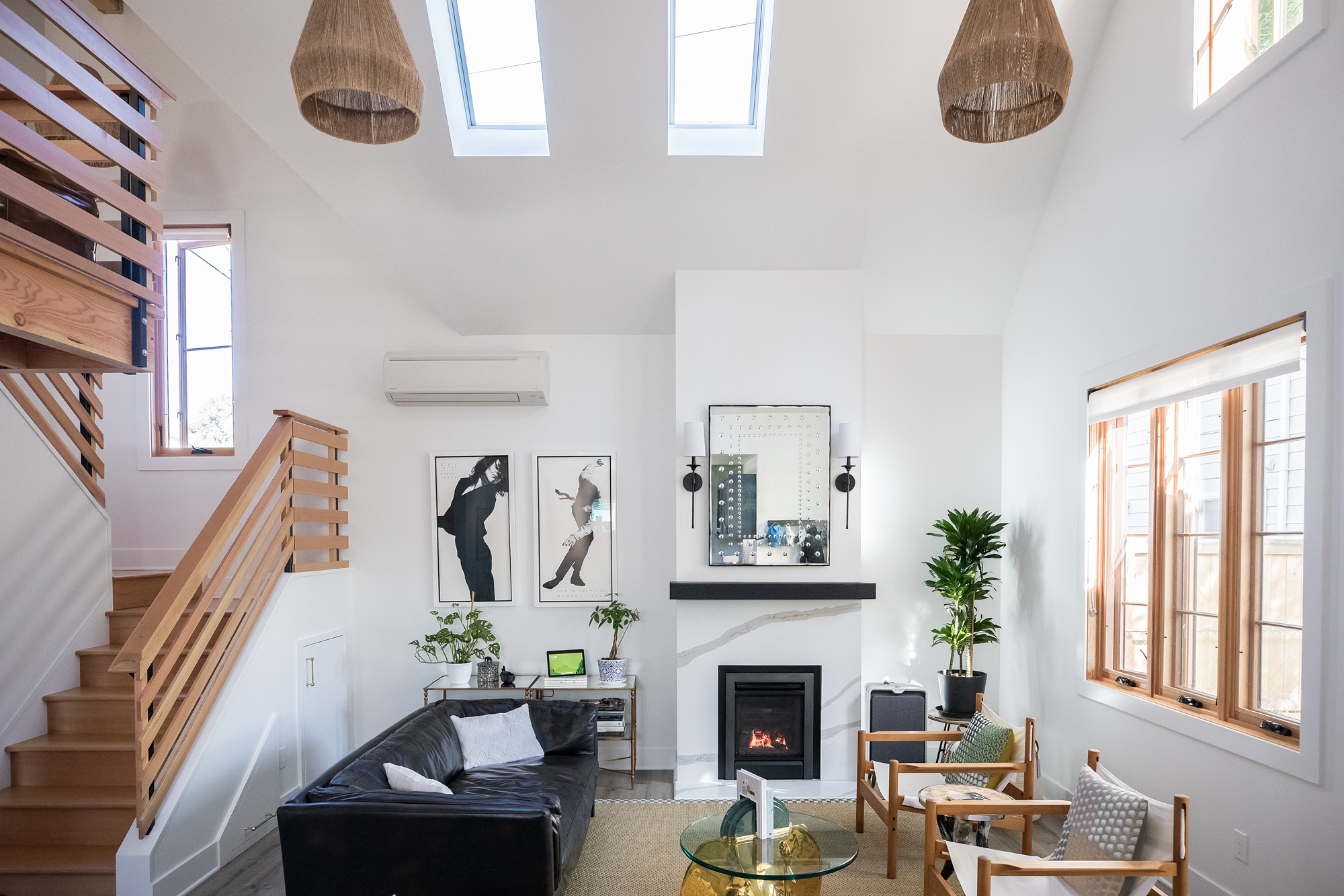 Looking down from the loft over the great room with skylights above, lit fireplace, stair railing, and two-story volume of the space, Vancouver Avenue ADU by Tweto Architecture
