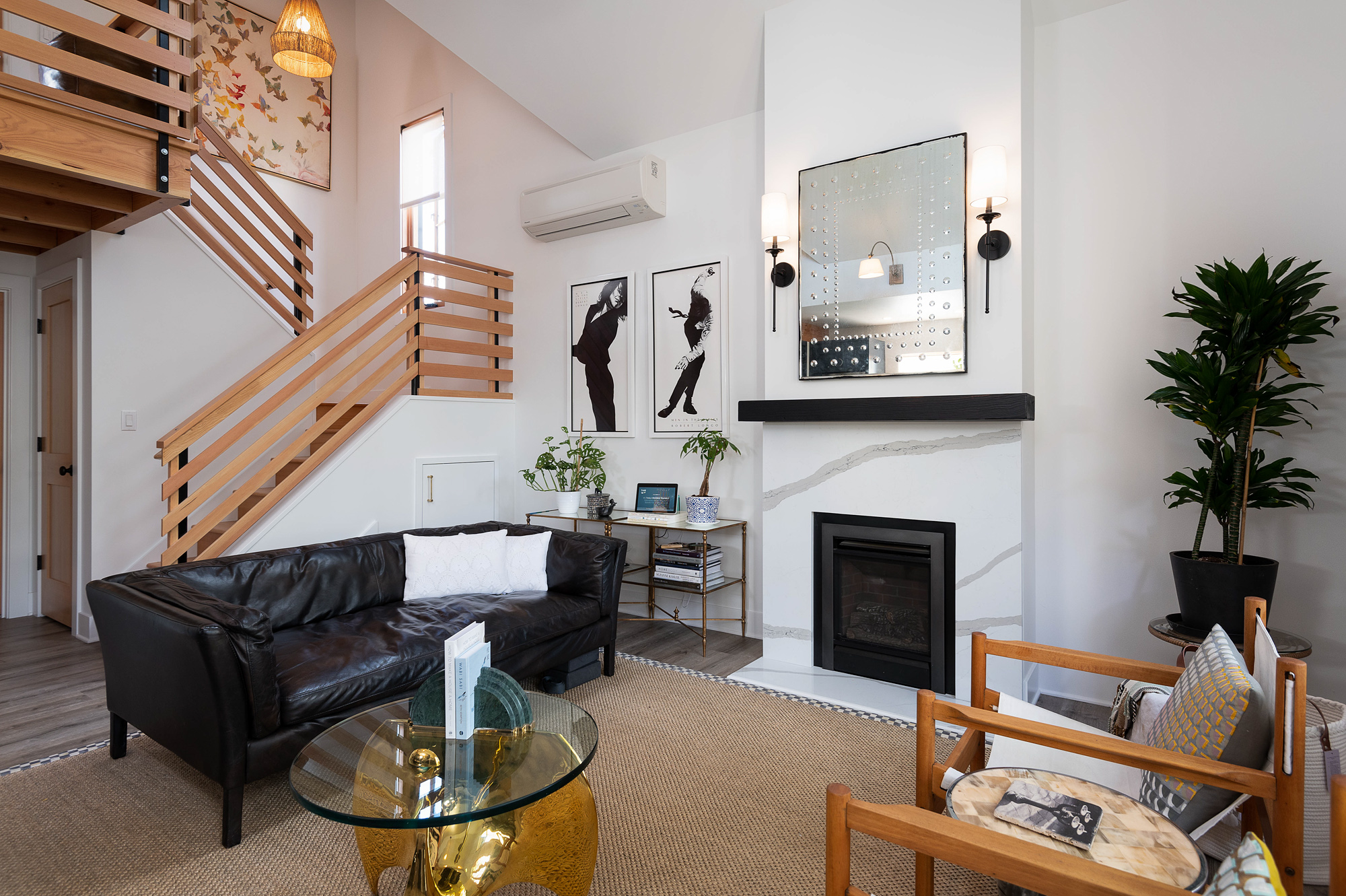 Living room with white quartz fireplace surround and black mantel, wood stair railing at left, black leather sofa, and wood-framed window with sheer curtain, Vancouver Avenue ADU by Tweto Architecture