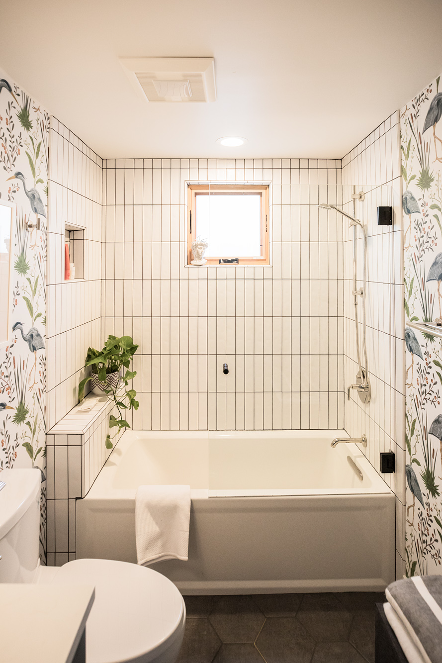 Bathroom looking at the tub, with vertical white subway tile, egret botanical wallpaper on either side, wood-framed window above the tub, Vancouver Avenue ADU by Tweto Architecture
